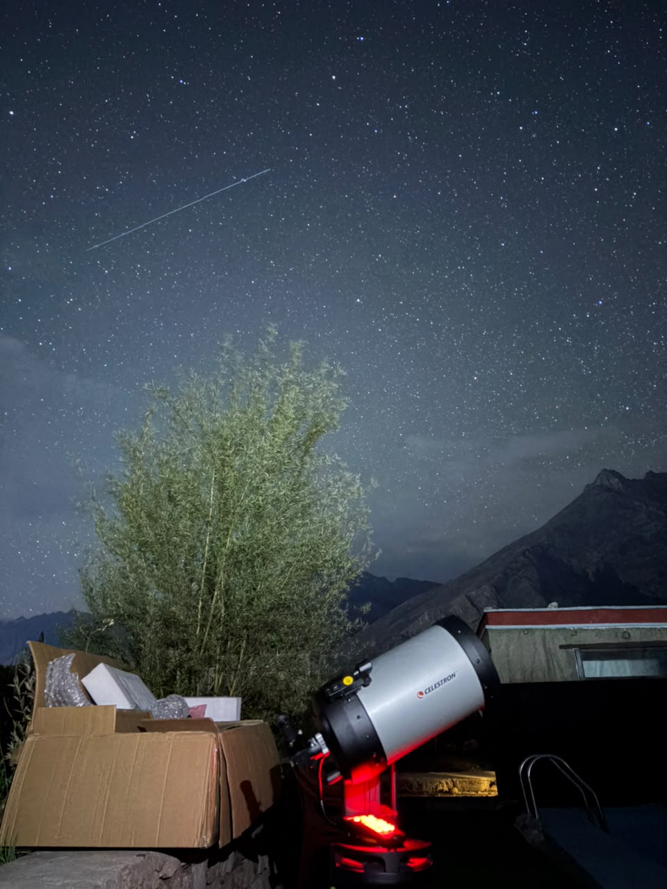 Celestron telescope set up under a star-filled Ladakh sky, a satellite trail crossing overhead