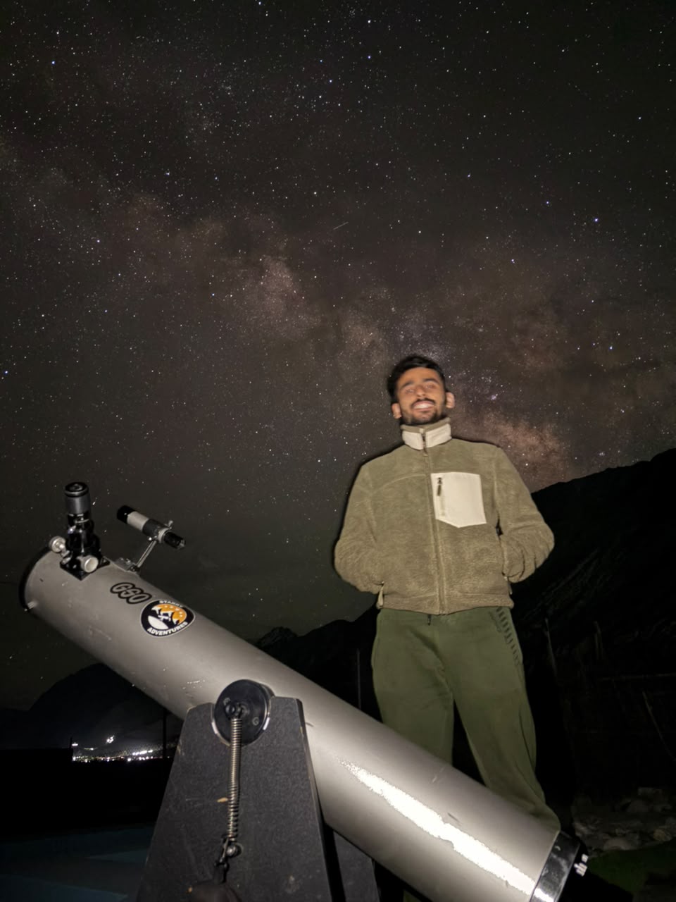 Guest smiling beside the telescope under the Milky Way at a Ladakh stargazing session