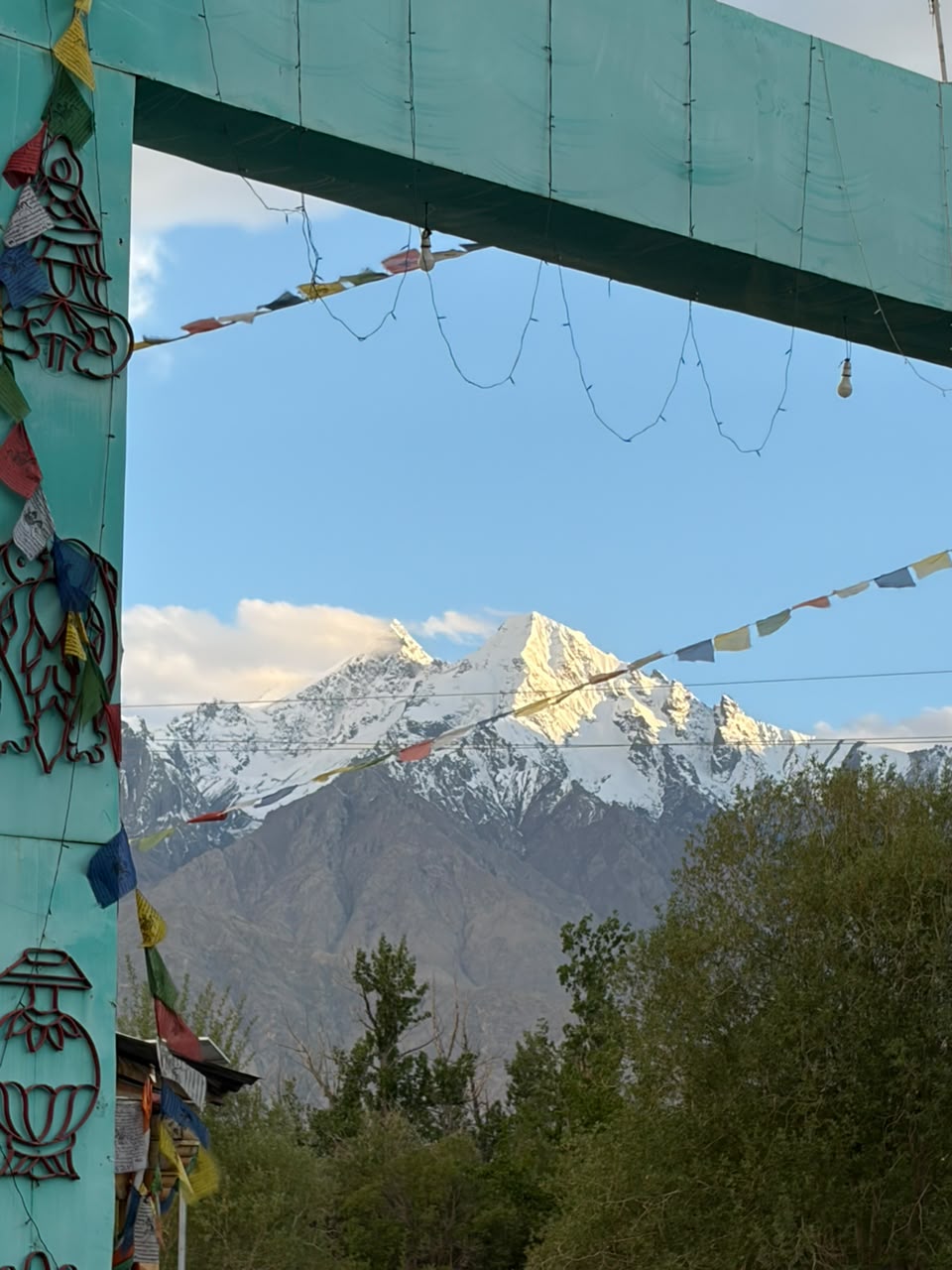 Snow-capped Ladakh peak framed by Buddhist prayer flags at a village gate